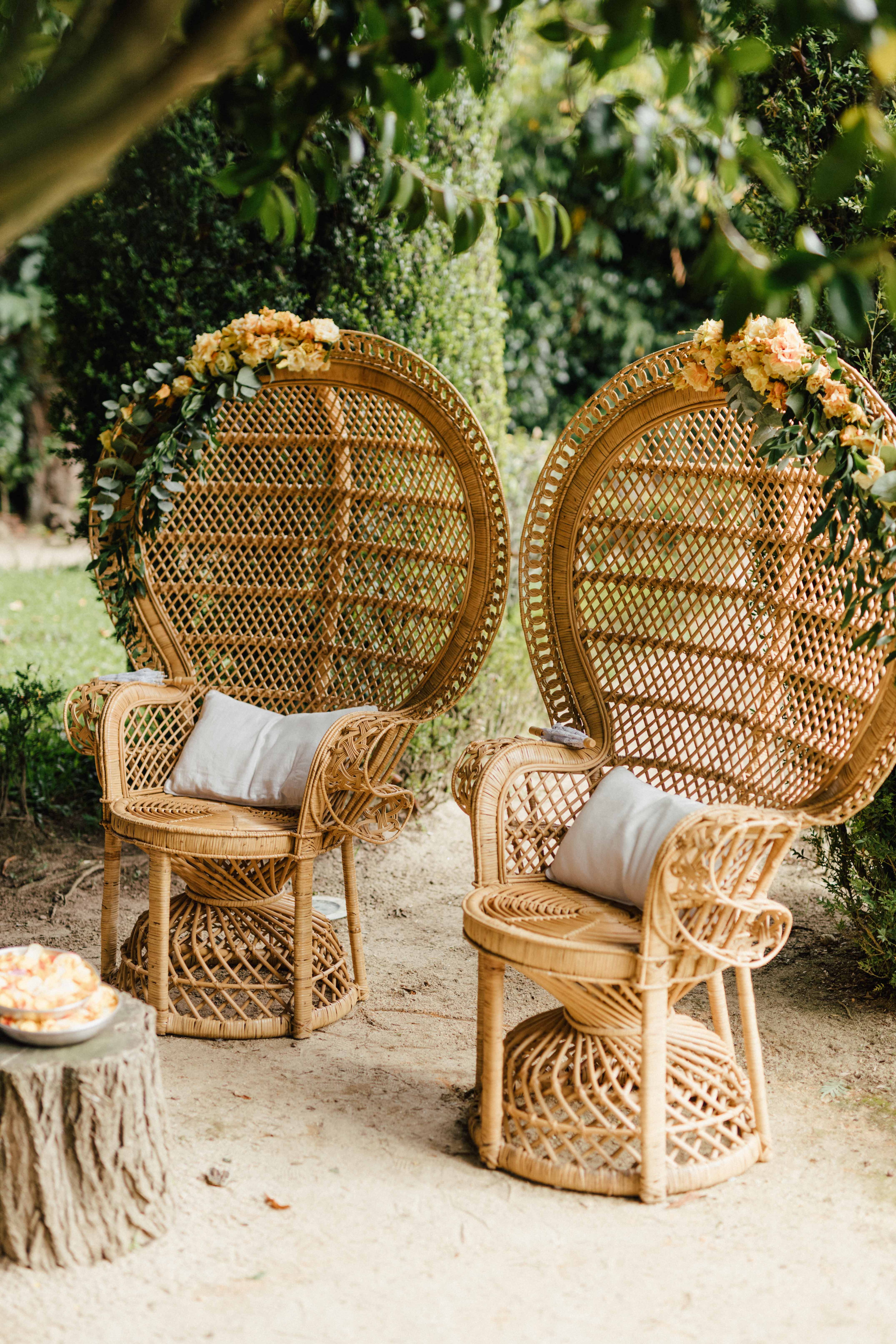 Duas cadeiras-trono em rattan coroadas de garlandas florais, sob a folhagem da quinta