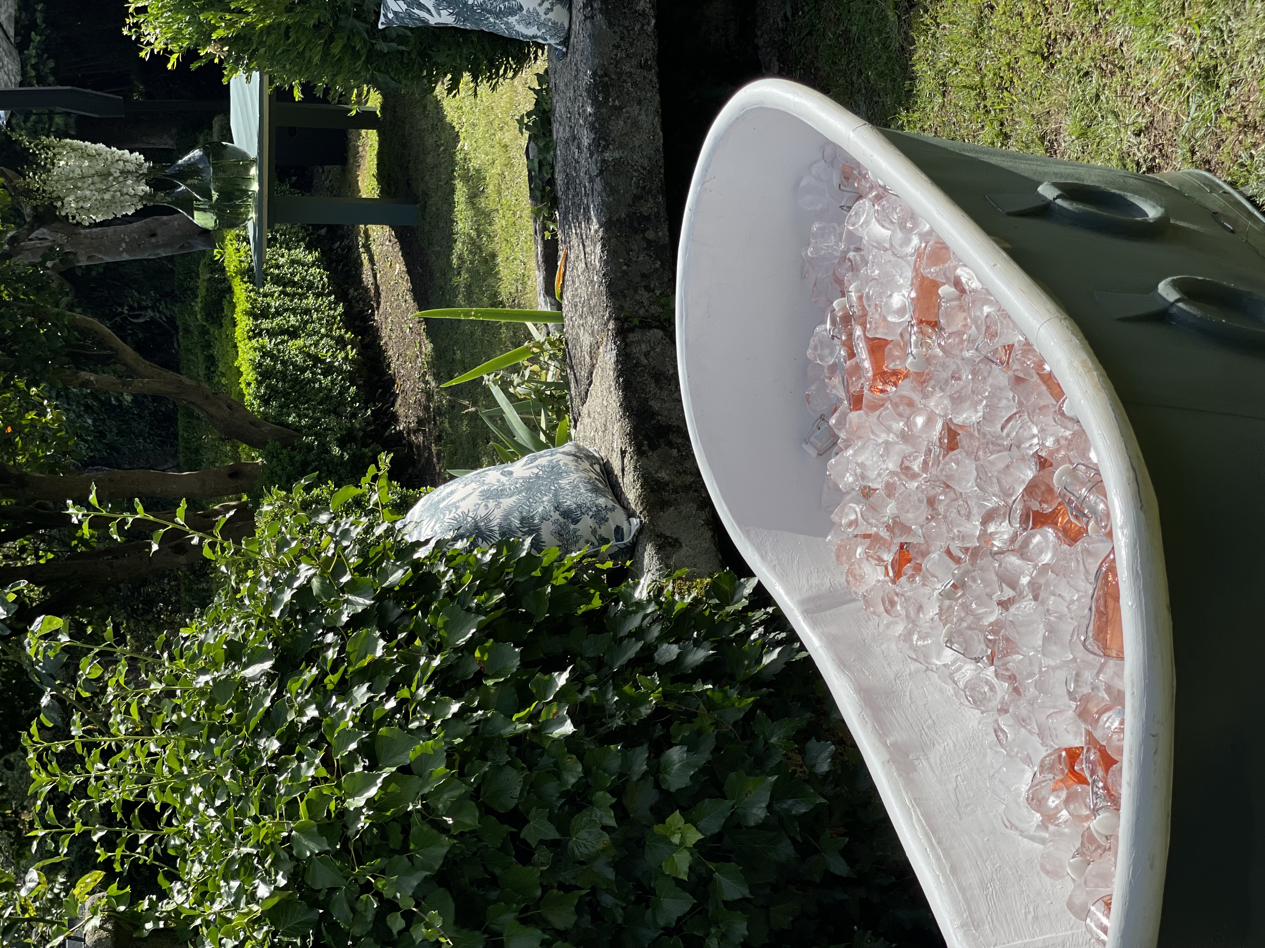 Vintage bathtub filled with ice and pink bottles in a garden setting.