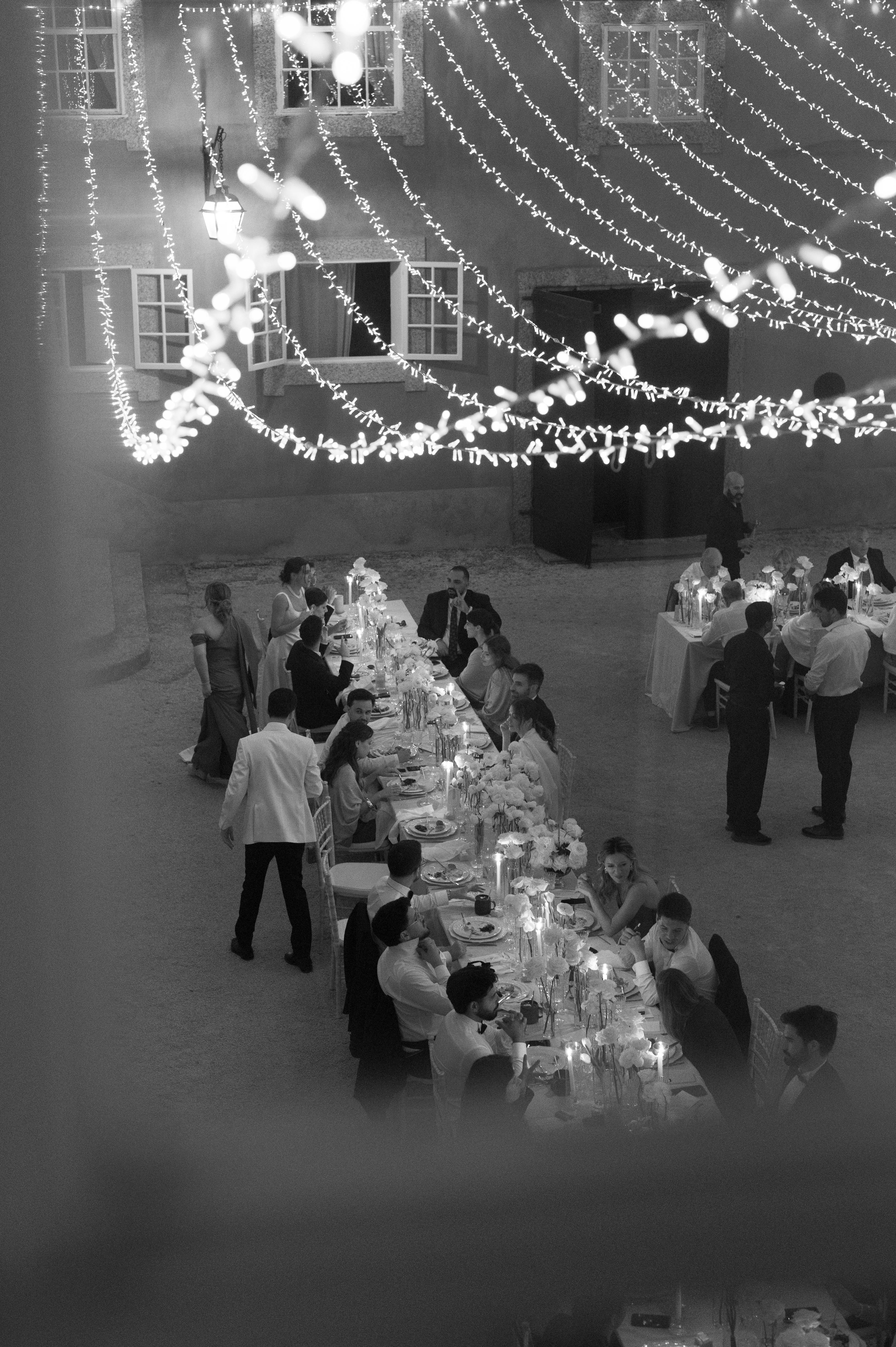 Vista aérea do pátio à noite, com fairy lights em arcos sobre o jantar, em preto e branco