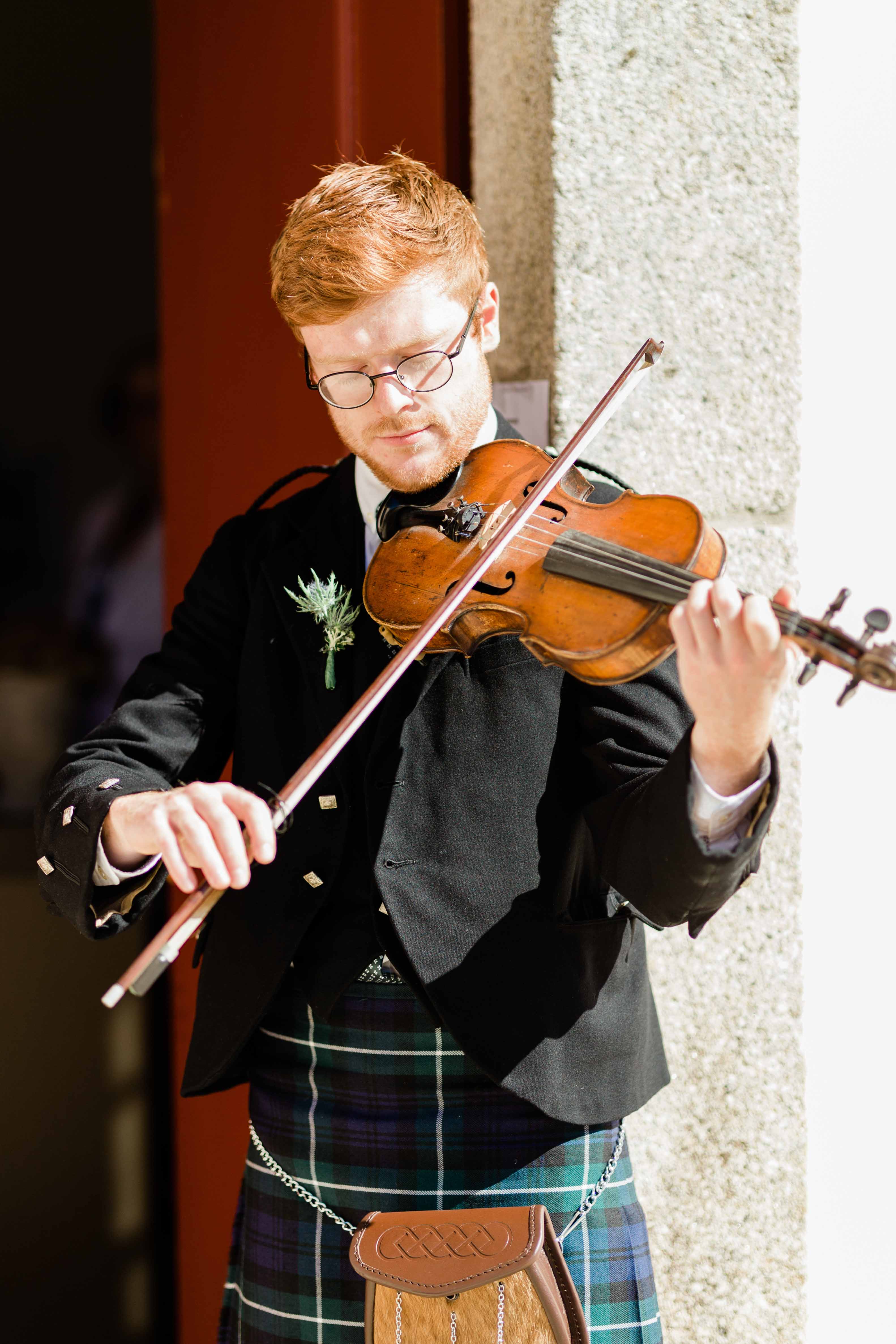 Violinista escocês em kilt, thistle no peito, a tocar à entrada da cerimónia