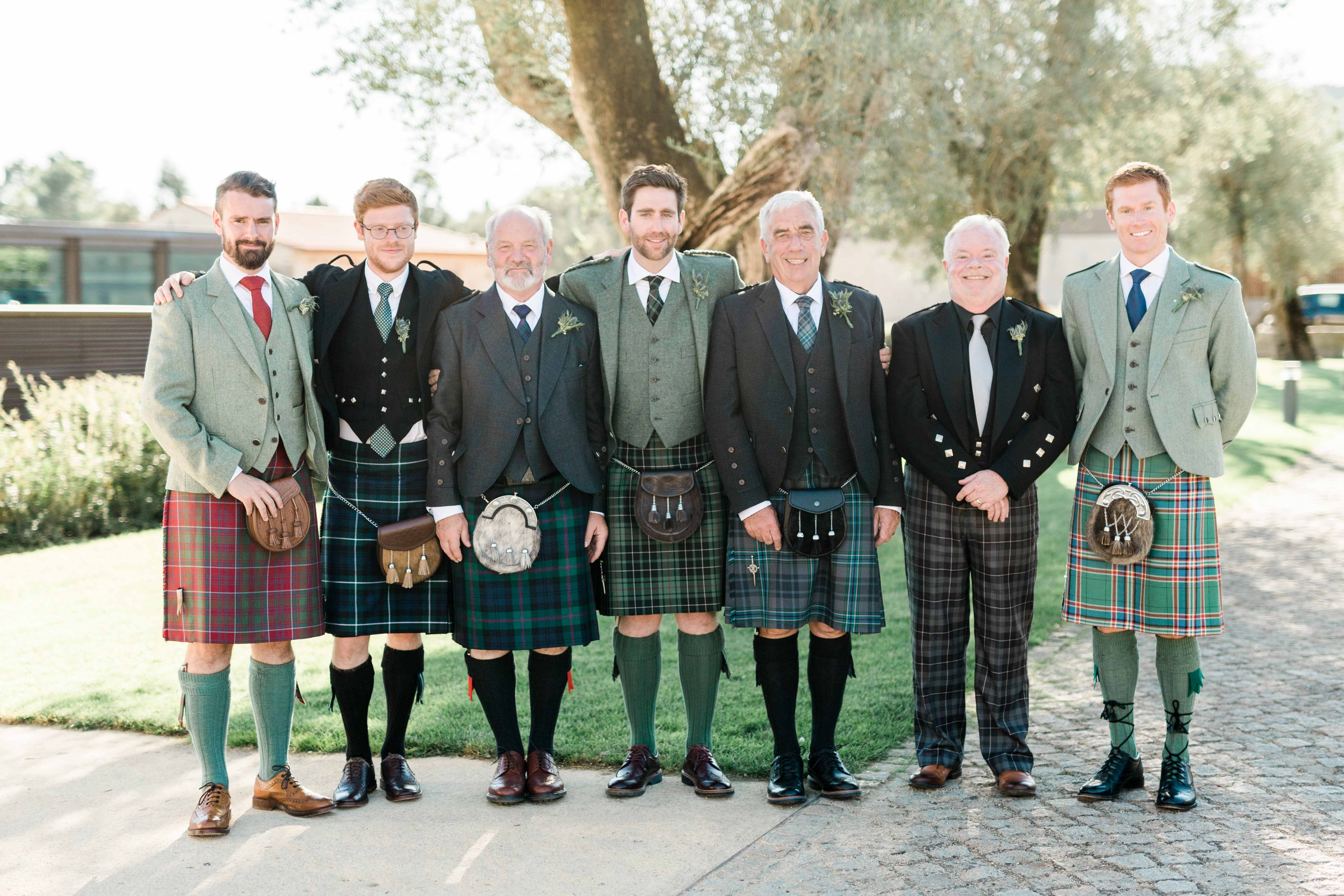 Sete homens da família em kilts e tartans diferentes, sob uma oliveira centenária