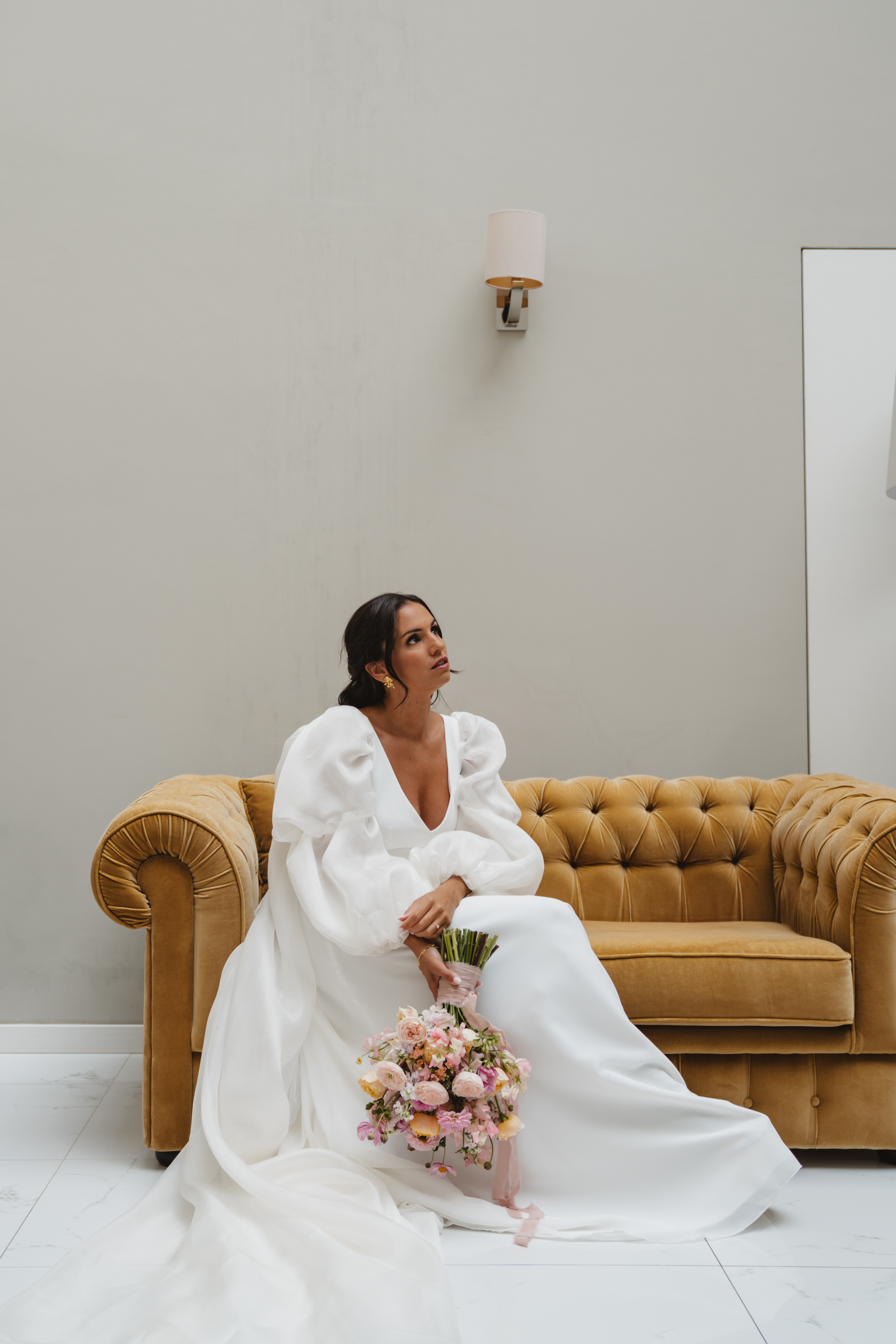 Patrícia sentada num sofá Chesterfield em veludo dourado, com vestido de organza e ramo de rosas garden