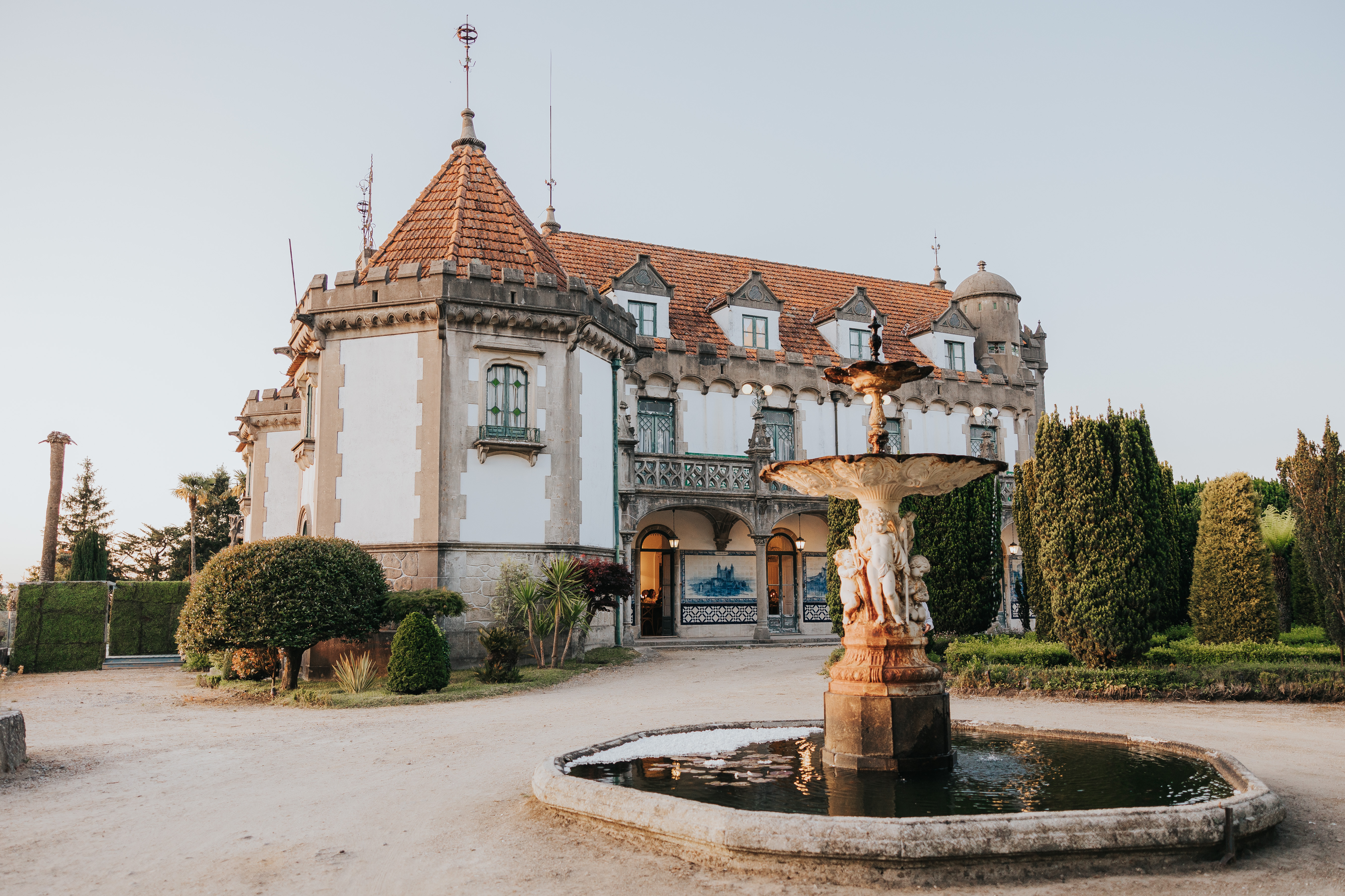 Castelo do Bom Jesus ao fim da tarde, com fonte de querubins em primeiro plano e a fachada neogótica em pedra ao fundo