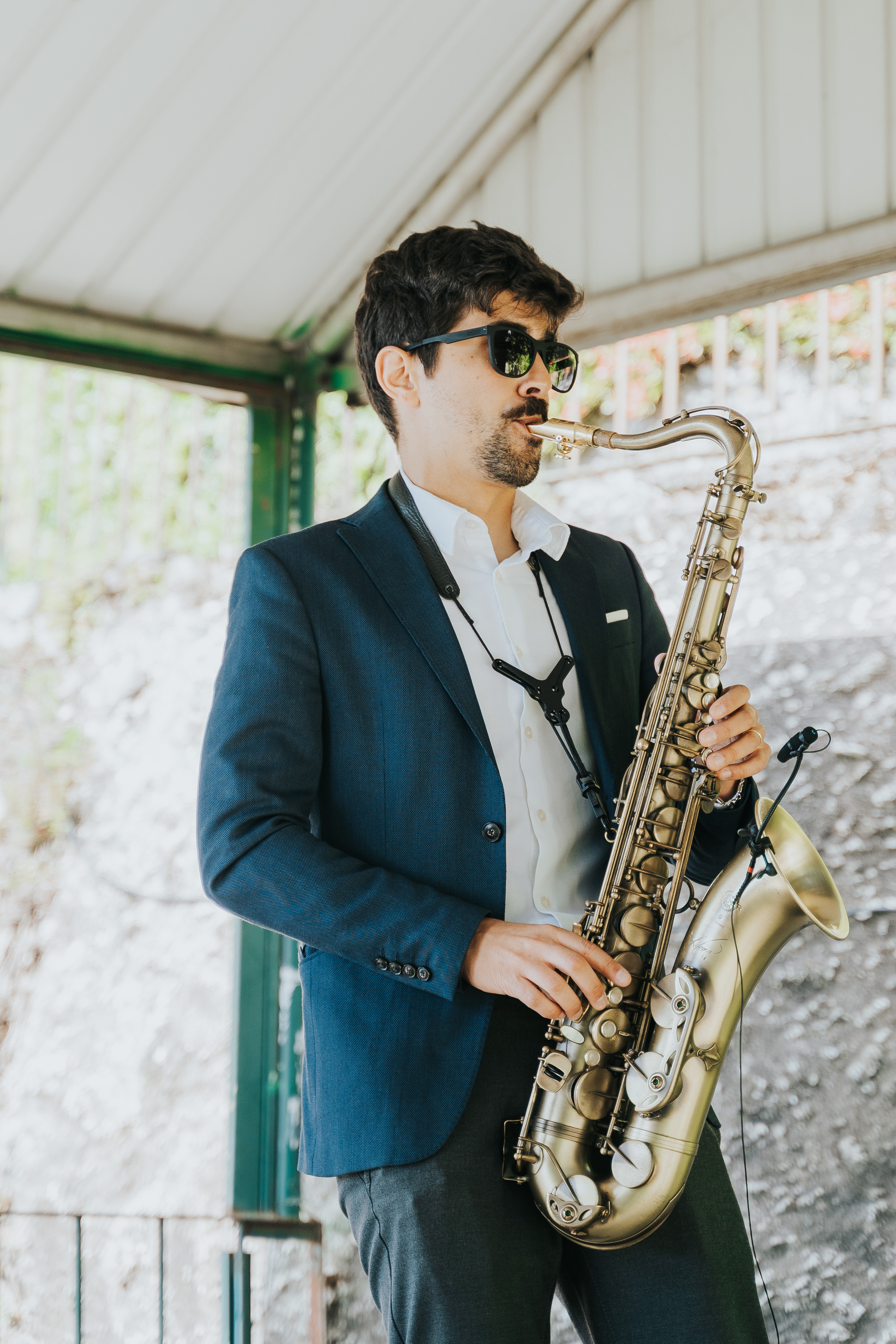 Saxofonista Samuel, de blazer azul e óculos escuros, a tocar saxofone tenor dourado durante o cocktail